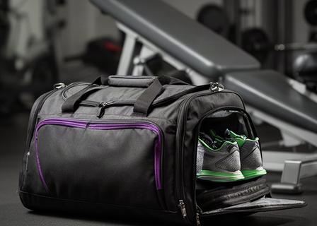 Compacte zwarte sporttas met schoenenvak naast een fitnessbank